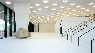 Foyer mit hohen Decken, einem Stützpfeiler auf einem grossen Stein und einem breiten Treppenaufgang.