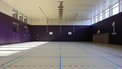 Leere Sporthalle mit farbig markiertem Boden und Basketballkörben.