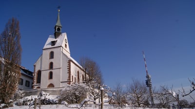 Kirche im Schnee mit Turm im Hintergrund unter blauem Himmel.",