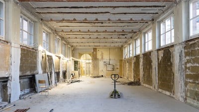 Verfallener Raum mit abgenutzten Wänden und Decke, leere Stühle und Palettenheber.