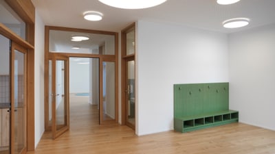Leerer Flur mit Holzboden und grüner Bank.