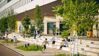 Menschen sitzen und gehen vor einem modernen Gebäude mit Bäumen.