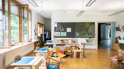 Klassenzimmer mit leeren Schreibtischen und Kunstwerken an der Wand.