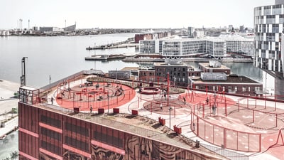 Dachspielplatz mit roter Ausstattung und Stadtblick am Wasser.