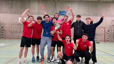 Jubelnde junge Männer in Sporttrikots, halten einen Pokal in einer Turnhalle hoch.