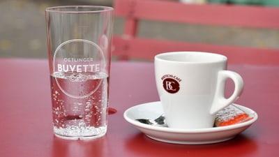 Nahaufnahme eines Glases und einer Kaffeetasse auf einem roten Tisch im Freien.