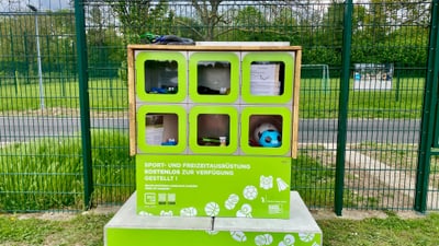 Grünes Schliessfach mit Sport- und Freizeitgeräten im Freien.