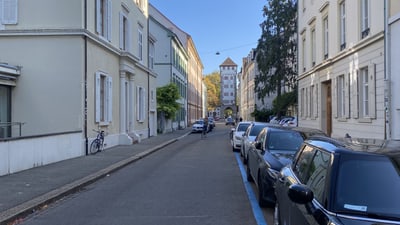 Strasse mit geparkten Autos und alten Gebäuden bei Tageslicht.