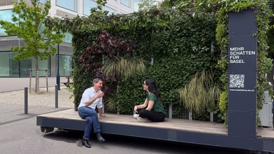 Zwei Personen sitzen vor einer begrünten Wand in der Stadt Basel.