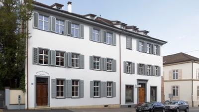 Weisses Gebäude mit grauen Fensterläden und geparkten Autos davor.