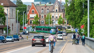 Strassenszene mit Velofahrenden, Zufussgehenden, Autos und einem Tram in Basel.