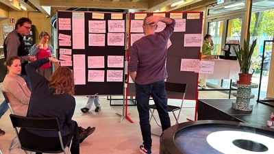 Personengruppe betrachtet Notizen auf Pinnwand in modernem Raum.