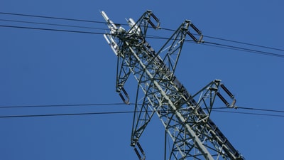 Strommast mit Hochspannungsleitungen gegen blauen Himmel.