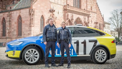 Zwei Polizisten stehen vor einem Polizei-Tesla auf dem Münsterplatz