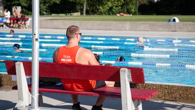 Rettungsschwimmer auf einer Bank beim Schwimmbad.