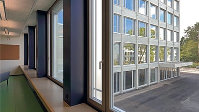 Fensterfront mit breiten Holz-Sims und durch das Fenster Sicht auf einen anderen Teil des Schulhauses.