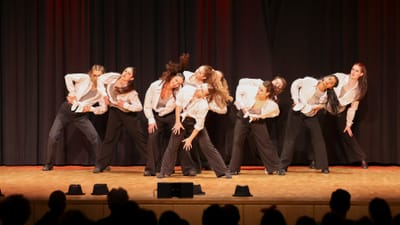 Gruppe von Tänzern auf einer Bühne in weisser Kleidung.