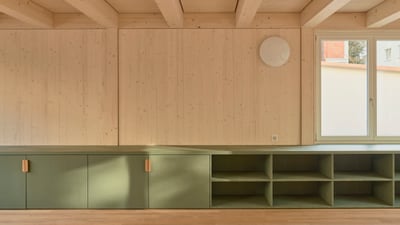 Innenansicht eines Raumes mit Holzwänden und Regalen unter einem Fenster.