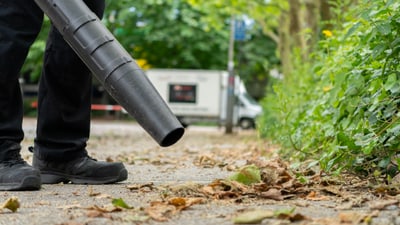 Arbeiter benutzt Laubbläser auf Gehweg.