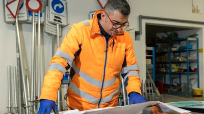 Mann in orangefarbener Sicherheitskleidung liest Pläne in Werkstatt.