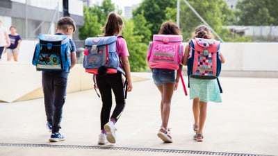 Vier Kinder mit Rucksäcken laufen nebeneinander.