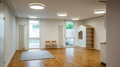 Leerer Raum mit Holzboden, Deckenlichtern und Spielbereich.