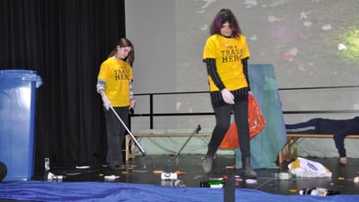 Zwei Personen in gelben T-Shirts räumen Müll auf der Bühne auf.",