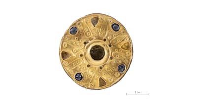 Runde mit grünen Granaten, blauem Glas und Goldauflagen verzierte Scheibenfibel und Massstab 1cm