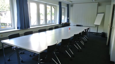 Leerer Konferenzraum mit langem Tisch und Stühlen.