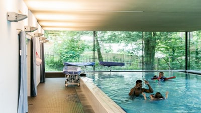 Menschen schwimmen in einem Innenpool mit grossen Fenstern.