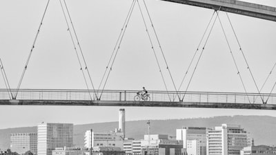 Radfahrer auf Brücke mit Stadt im Hintergrund.