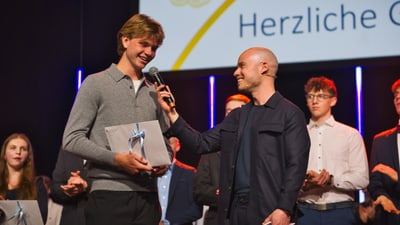 Mann interviewt jungen Mann bei Preisverleihung auf Bühne.