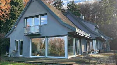 Modernes Haus mit grauer Fassade und grossen Fenstern, umgeben von Bäumen.