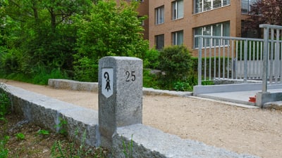 Steinmarkierung mit der Zahl 25 auf einem Schotterweg neben einem Gebäude.