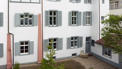 Weisses historisches Gebäude mit grauen Fensterläden und Ziegeldach.