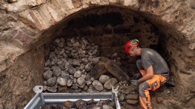 Archäologe mit Baustellenhelm in der Steinkammer-Luftheizung, die Feldsteine in eine Kiste legt.