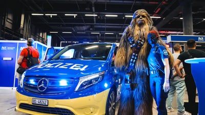 Person in Star Wars Kostüm neben Polizeiauto auf Messe.
