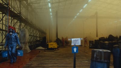 Industriearbeiter in Schutzanzügen in einer Fabrikhalle mit Gerüsten.