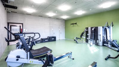 Helle, leere Sporthalle mit Fitnessgeräten und grün gestrichener Wand.