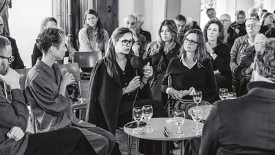 Frau spricht in einem Podiumsgespräch mit Publikum im Hintergrund.