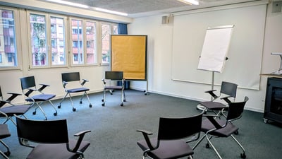 Leerer Seminarraum mit Stuhlkreis und Flipchart.