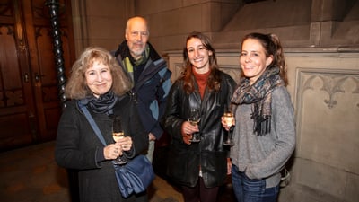 Vier lächelnde Personen mit Getränken in einem Raum mit gotischer Architektur.