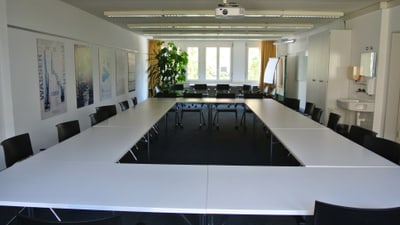 Konferenzraum mit Tischen in U-Form und Projektor an der Decke.