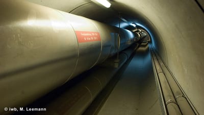 Tunnel mit grossen Rohren und Beleuchtung.