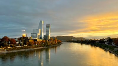 Blick auf den Rhein bei Abenddämmerung mit den Roche-Türmen im Hintergrund.