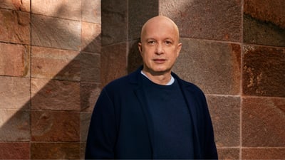 Person in dunkler Kleidung steht vor einer Steinmauer.