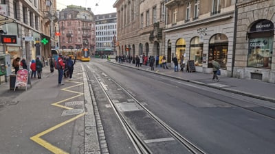 Strassenszene mit Strassenbahn und Fussgängern auf Gehweg in Basel.",