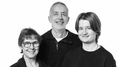 Drei lächelnde Personen in schwarzer Kleidung vor weissem Hintergrund.