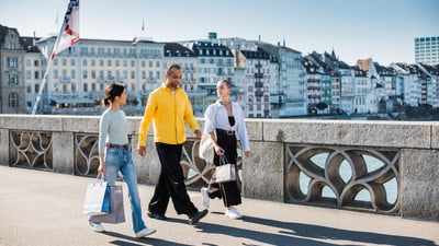 Drei Menschen gehen über eine Brücke mit Altstadt im Hintergrund.