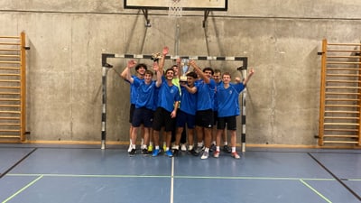 Jubelnde junge Männer in Sporttrikots, halten einen Pokal in einer Turnhalle hoch.